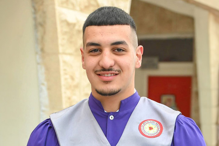 Amir-Jamal-Al-Daraawi, ein Jugendlicher mit kurzen dunklen Haaren und kurzem Bart, trägt eine Robe mit dem Logo der Evangelischen Schule in Beit Sahour.