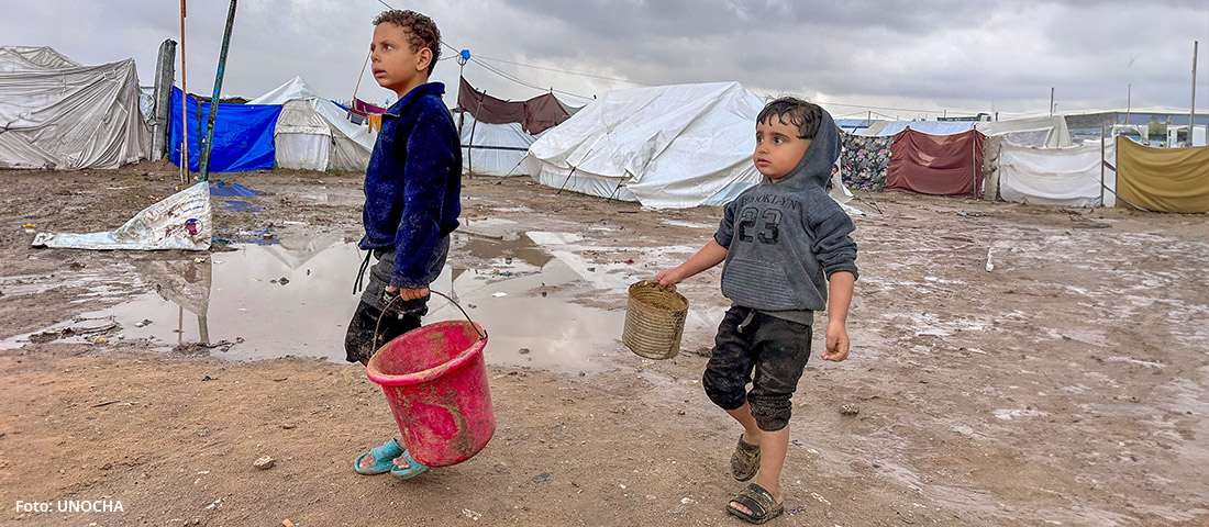Zwei Jungen sind in einem verregneten Flüchtlingslager in Gaza mit Eimern unterwegs. Foto: UNOCHA