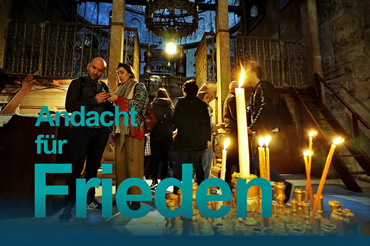 Im Vordergrund brennen mehrere Kerzen. Im Hintergrund stehen mehrere Menschen in einem sakralen Raum. Foto: Nils Clausen