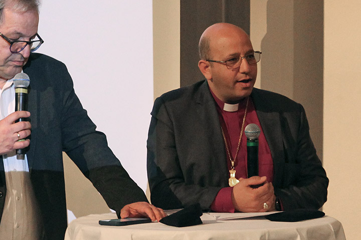 Bischof Haddad steht an einem Stehtisch und hält ein Mikrophon in der Hand. Daneben steht Matthias Wolf.