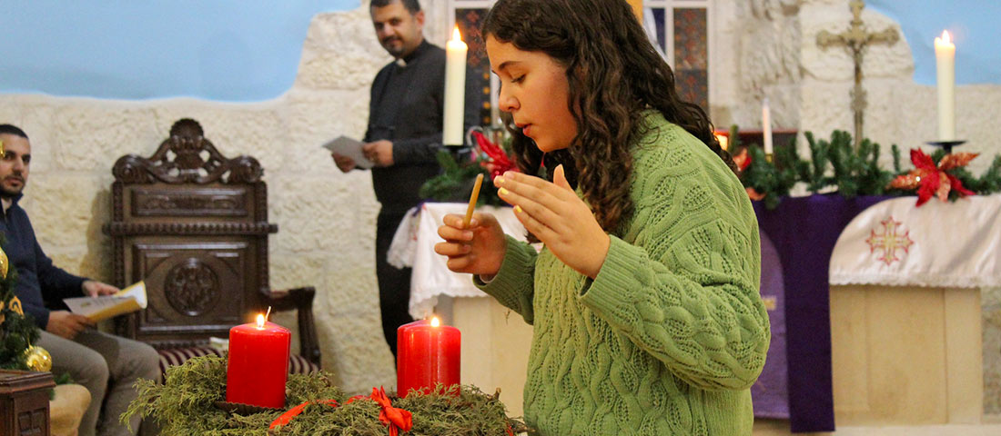 Eine junge Christin der ELCJHL zündet im Altarraum der Reformationskirche Beit jala Kerzen auf einem Adventskranz an. Sie trägt einen grünen Pullover und bläst gerade das Streicholz aus.