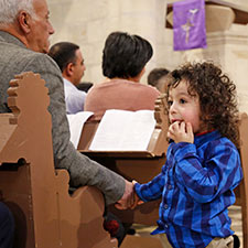 In einer evangelischen Kirche in Palästina: ein alter Mann sitzt auf einer Kirchenbank, davor steht ein kleiner Junge mit dunklen lockigen Haaren. Beide fassen sich an der hand.