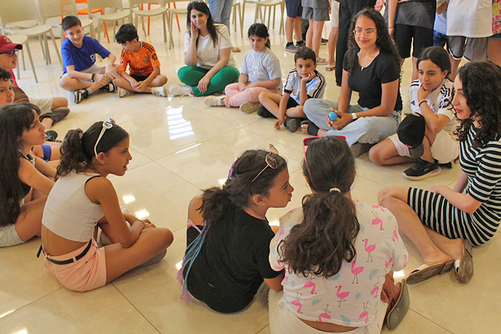 Auf einer Freizeit der ELCJHL in Jericho sitzen ein dutzend Kinder, Mädchen und Jungen, zusammen mit zwei Frauen im Kreis in einem Raum 