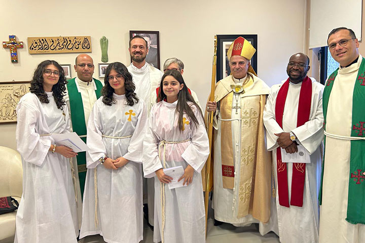 Drei Konfirmandinnen aus Amman im Vordergrund mit weißen Gewändern, dahinter stehen Bischof Azar (ELCJHL) in vollem Ornat, Pfarrer Hadad und weitere geistliche 