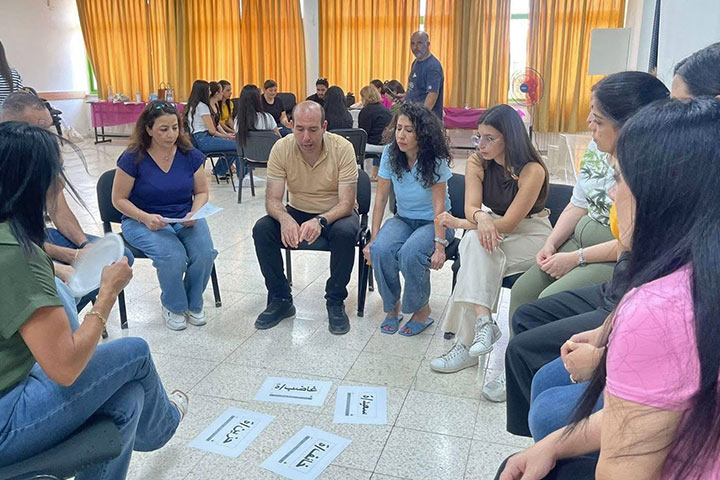 Lehrerinnen und Lehrer sitzen im Kreis und betrachten beschriebene Zettel auf der Erde