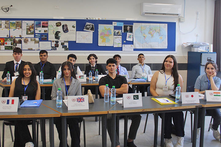 Jugendliche Schülerinnen und Schüler sitzen im Klassenraum, vor ihnen steht jeweils ein Schild mit einer Landesflagge