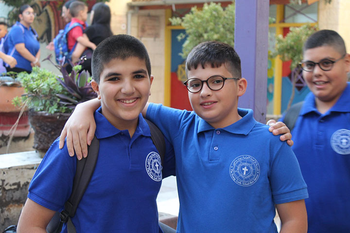 Zwei Schüler, etwa 12 Jahre alt, umarmen auf dem Schulhof ihre Schultern. Sie tragen blaue Polo-Shirts mit dem weißen Logo der Schule in Beit Sahour.
